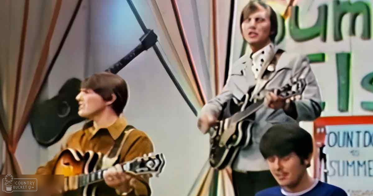 Three young adult males in a musical performance setting with microphones and colorful curtains, suggesting an indoor studio or stage environment.