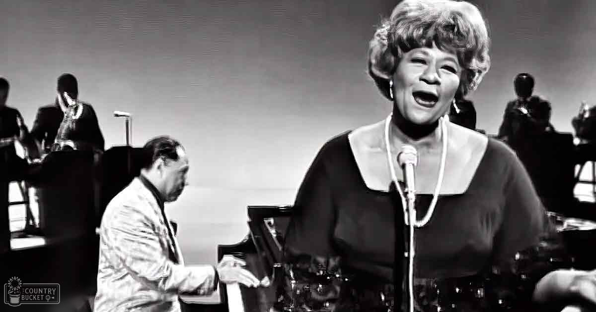 Middle-aged woman singing on stage with a pianist and background musicians; scene set in an indoor music hall or concert venue from the mid-20th century, dimly lit with spotlights focusing on performers.