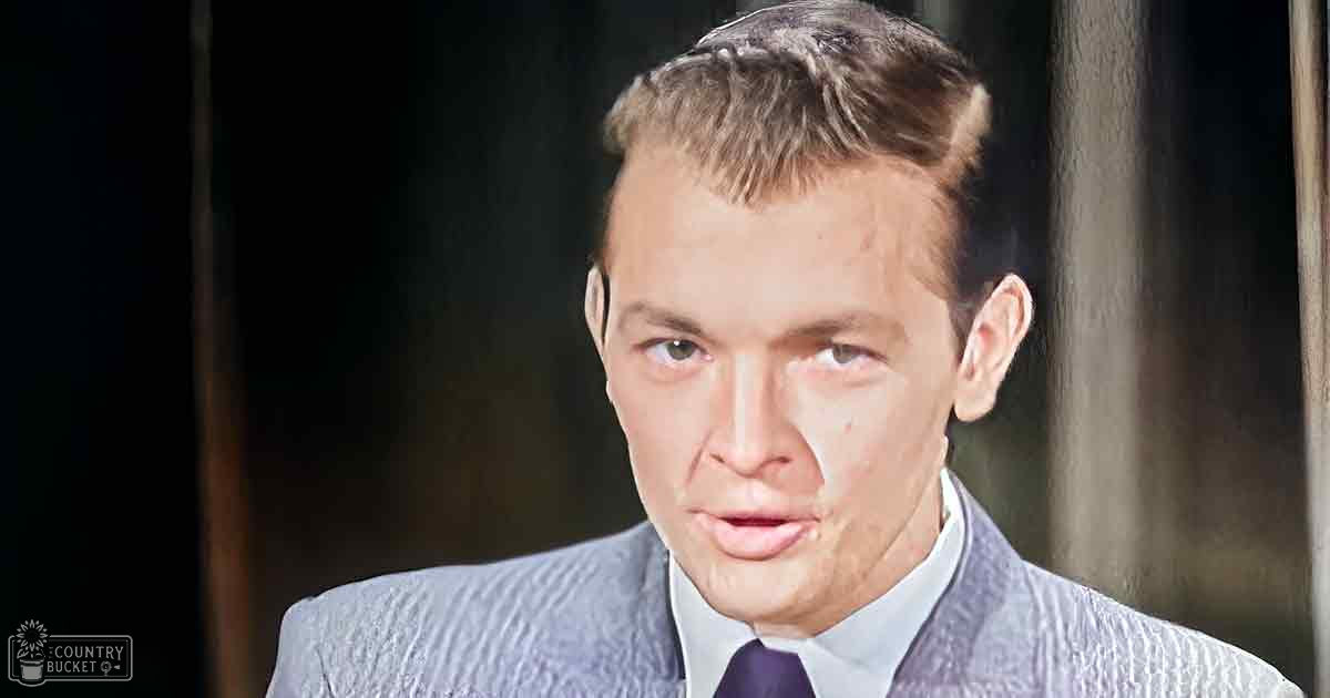 A young adult male wearing a tailored mid-20th-century suit jacket with textured light gray fabric stands against an indoor dark background, likely from the 1940s or 1950s.
