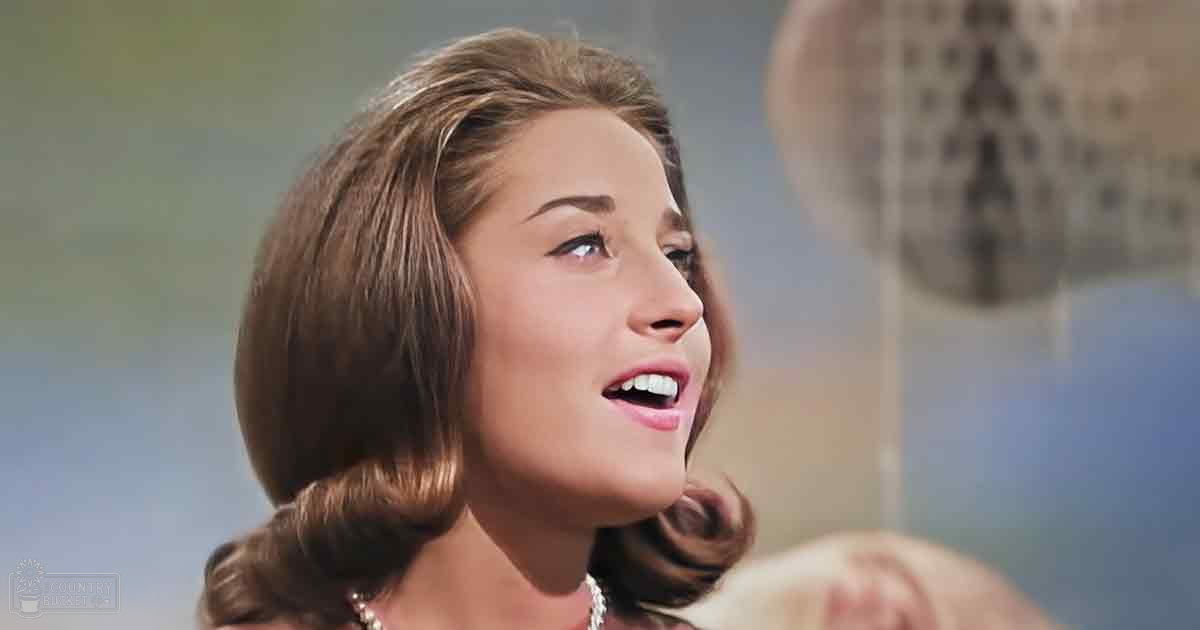 A young adult female wearing a fitted dark dress indoors, soft lighting suggesting daytime or indoor event setting.