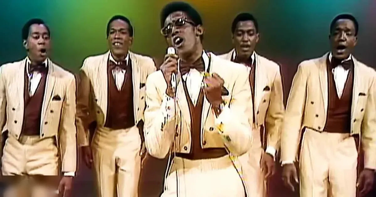 Adult male singers performing on stage at a concert setting with spotlights and colored lights.