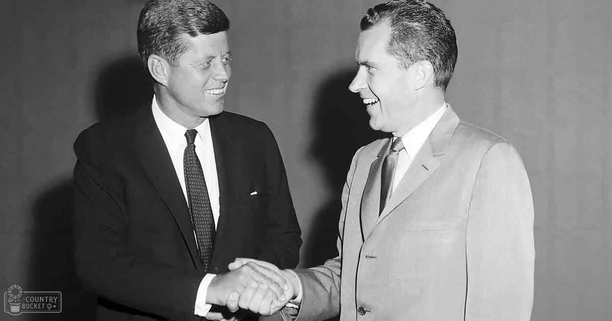 Two adults shaking hands in a formal indoor setting with plain backdrop; black-and-white photograph