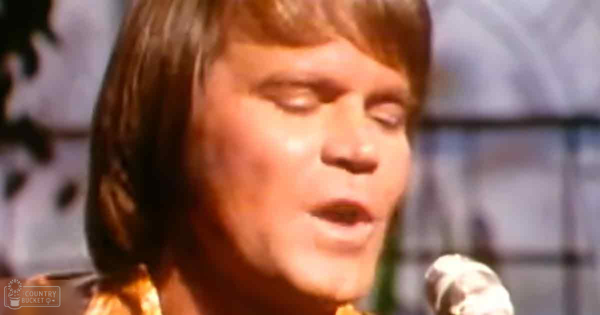 A young adult male singer wearing a patterned shirt or jacket with high collar performing into a microphone in an indoor performance setting.