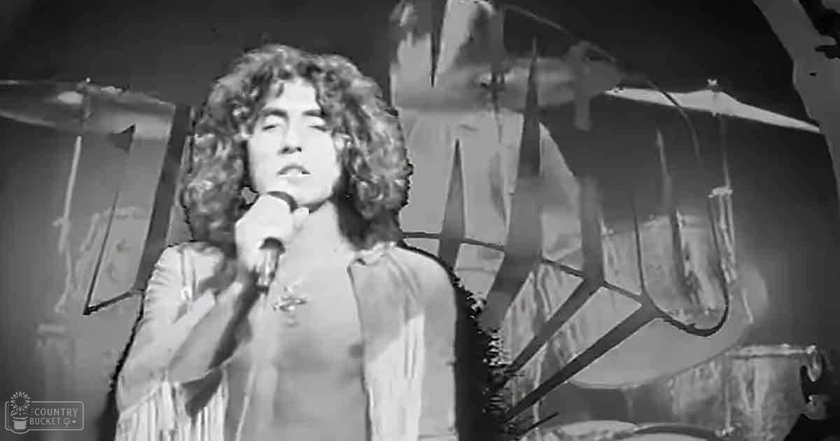 A young adult male shirtless performer on stage in a concert setting with a fringed garment over his shoulders.