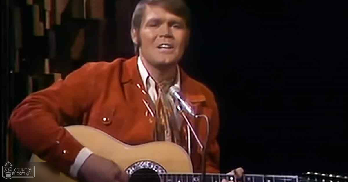 Adult male in orange double-breasted jacket and white shirt performing music, holding acoustic guitar in dimly lit studio or stage setting with microphone stand, 'Madly Didd' text on sleeve.
