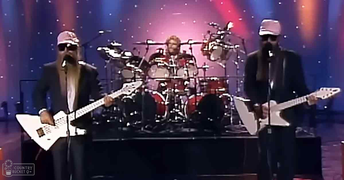 A concert scene with two guitarists playing electric guitars on stage under spotlights against a dark backdrop.