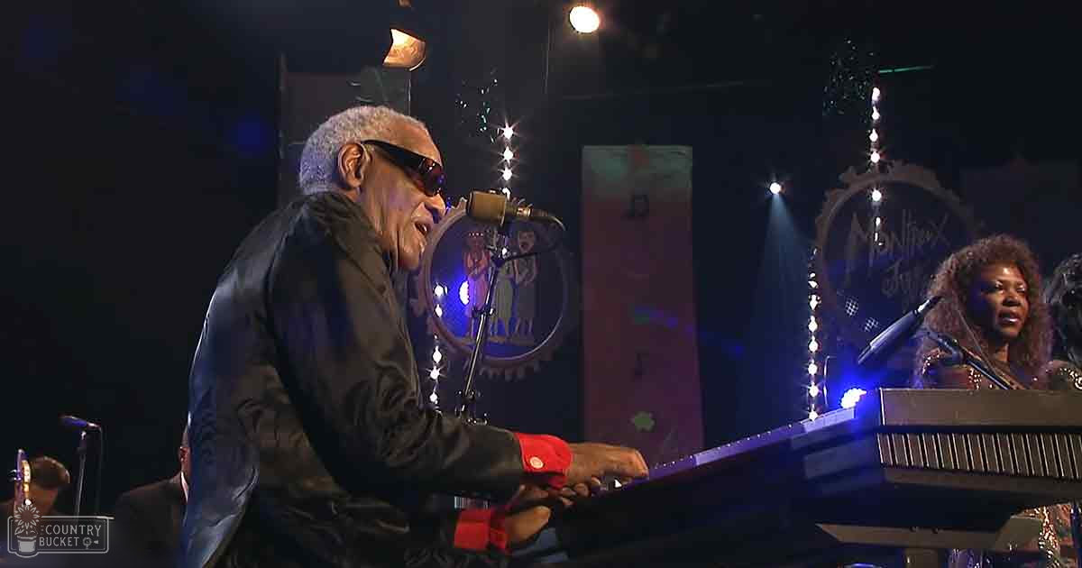 A middle-aged male piano player in a dark jacket with red cuffs and black shirt, accompanied by an adult female singer wearing a shiny dark outfit, performing on stage at the Montreux Jazz Festival under dim lighting.