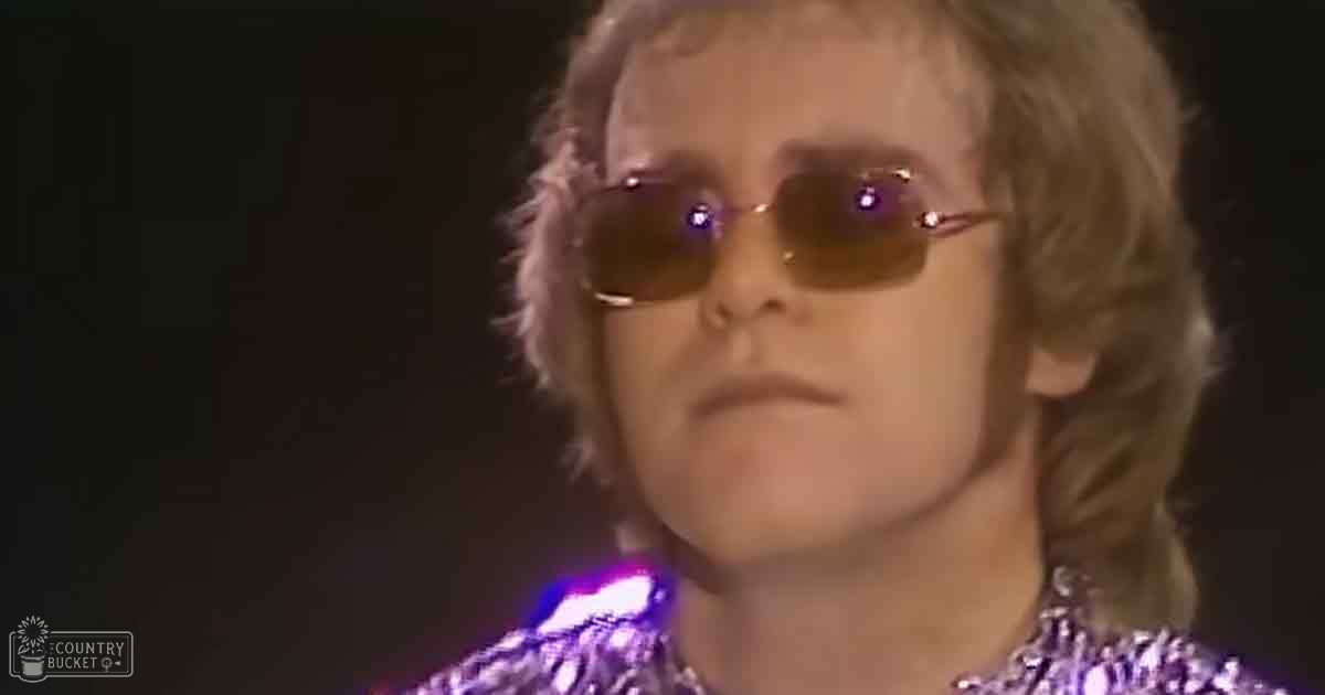 Adult male singer in a sparkly, sequined 1970s or 80s costume performing on stage with focused lighting and 'Madly Odd' text watermark.