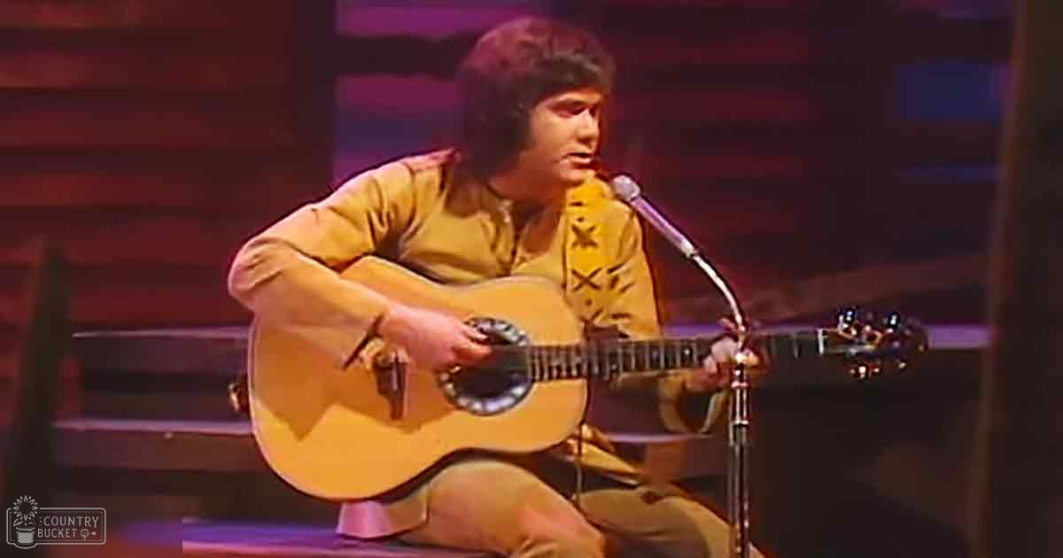 Young adult male wearing a star-patterned, long-sleeved button-up shirt and playing guitar in a studio setting with controlled artificial lighting.