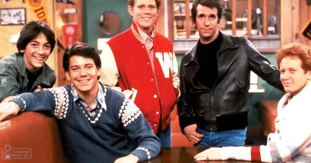 A group of five teenage boys and an adult man in a casual indoor setting, wearing jackets with distinct patterns and colors.