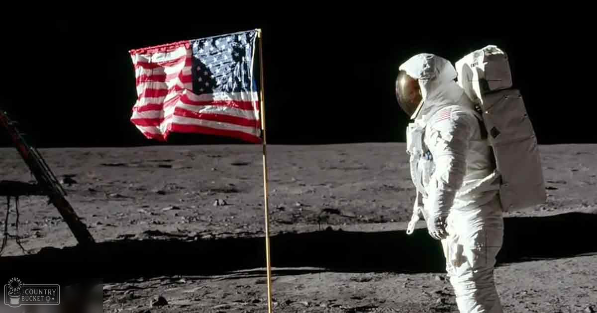 Astronaut in a space suit standing near an American flag on the moon's surface at night.