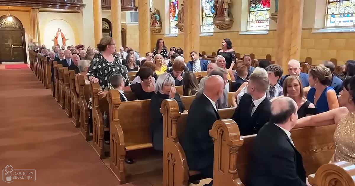 A wedding ceremony in progress inside a church with wooden pews, stained glass windows, and attendees dressed formally in suits and dresses.