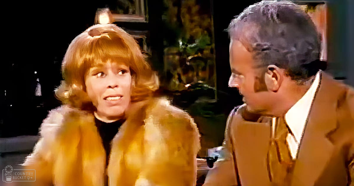 A woman in an indoor setting wearing a fur coat with a high collar, and a man in a light brown suit jacket over a white shirt and tie.