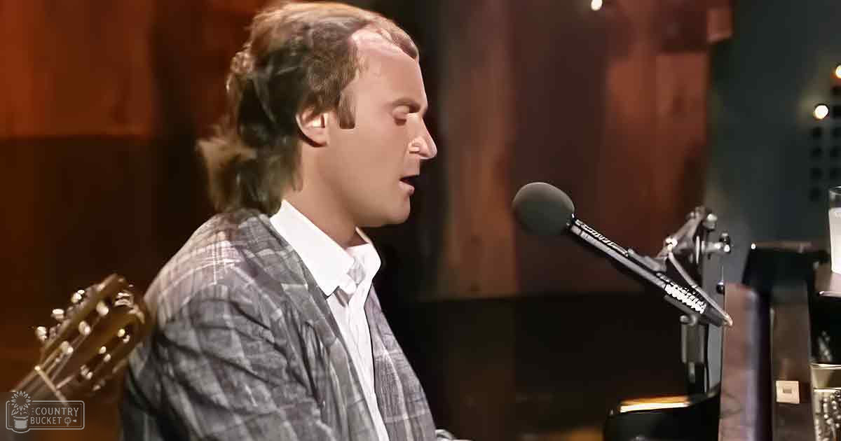 Young adult male in plaid blazer and white collared shirt performing in indoor music studio with wooden paneling and warm lighting.