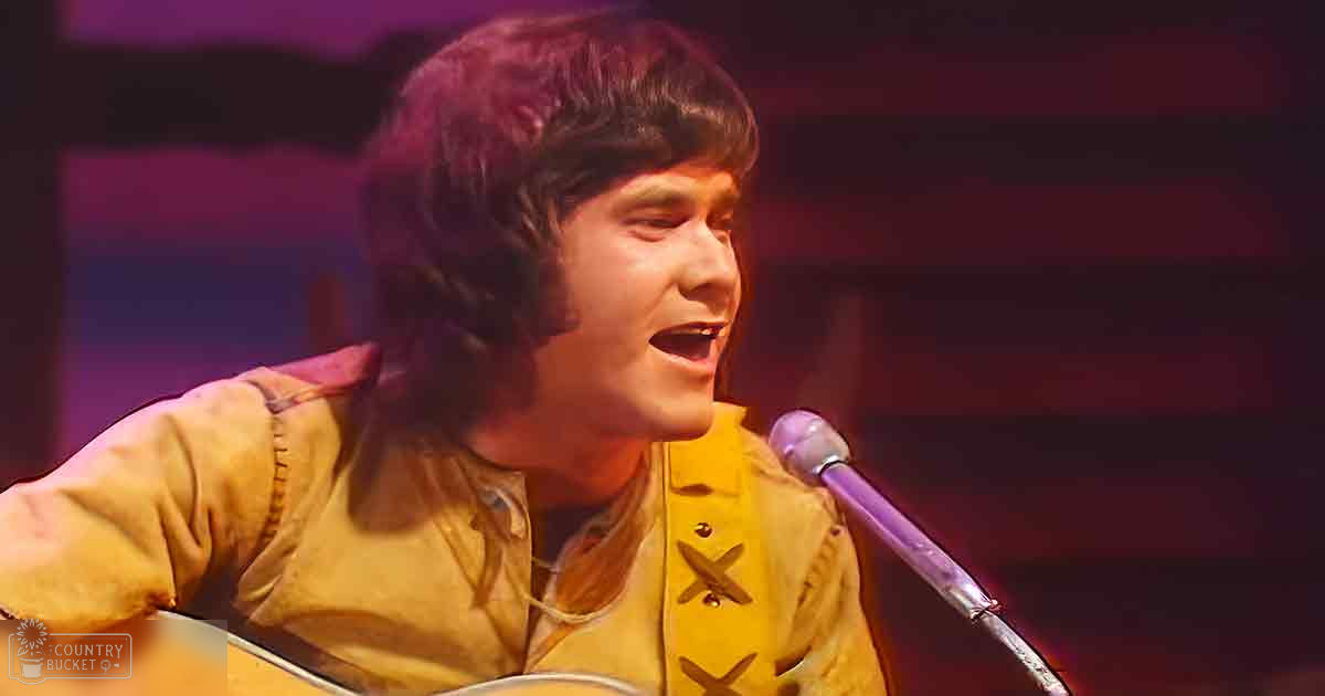 A young adult male singer wearing a long-sleeved, collared, yellow shirt with red accents on stage.