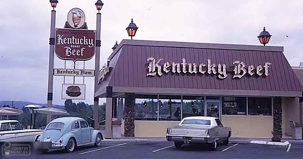 Two vintage cars parked outside a Kentucky Beef restaurant with overcast sky suggesting early evening or cloudy day; muted tones dominate the scene.