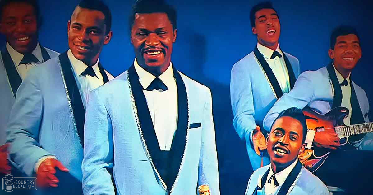 Young adults in light blue suits with black lapels and trim perform on a stage against a solid blue background.