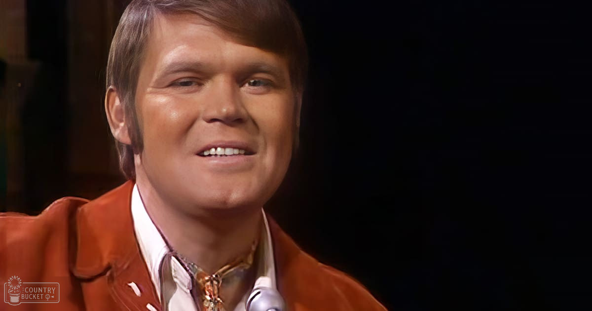 Young adult male wearing a red leather jacket with white collar, relaxed fit, likely 1970s style, indoors with dark background lighting.