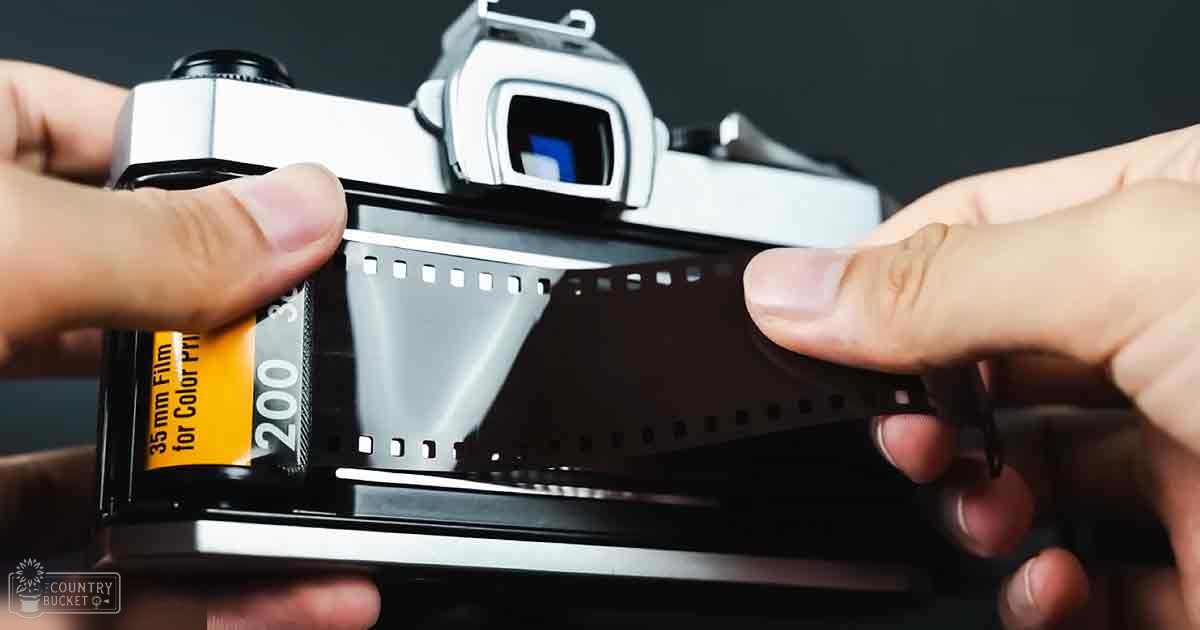 An adult male handling 35mm film with an analog camera in what appears to be an indoor setting with controlled lighting.