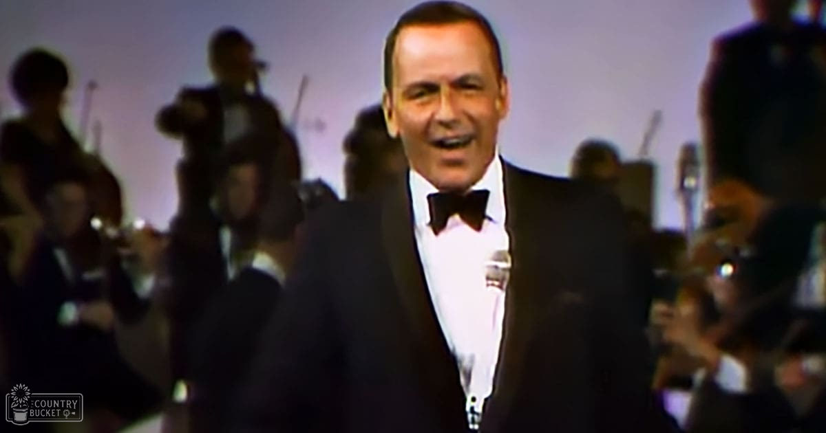 Adult male performer in a formal black tuxedo with white shirt and bow tie on stage under focused lighting during an indoor concert or performance.