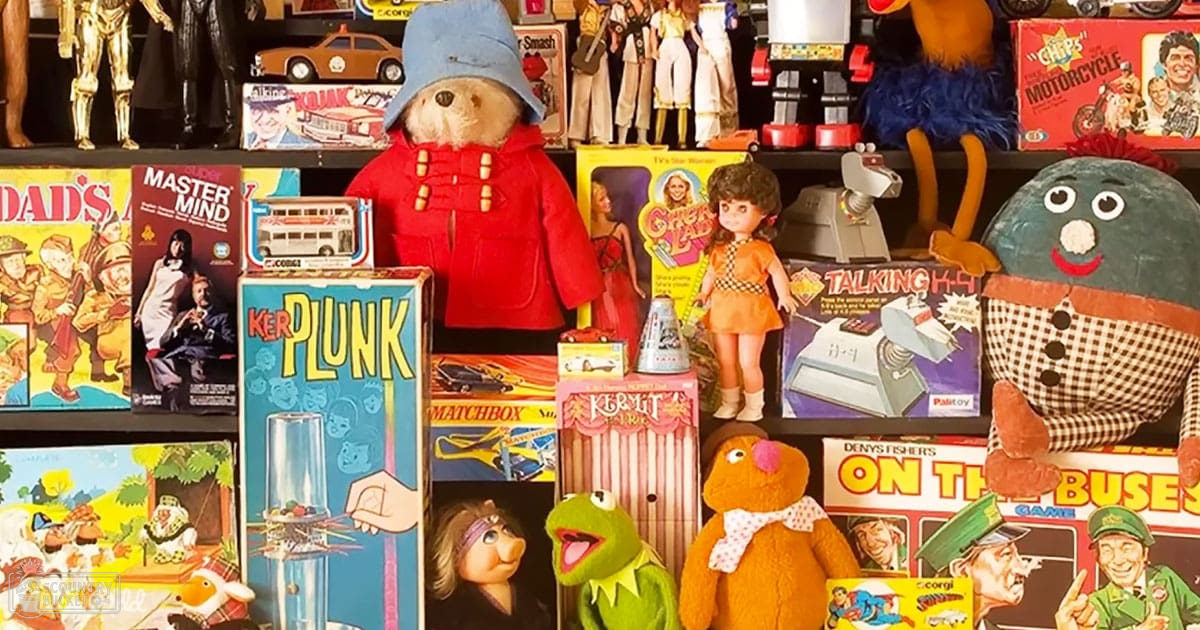 Vintage toys and games displayed in a store or collector's display area; colorful assortment including Paddington Bear, Kermit the Frog, Fozzie Bear, Gumby, board games like 'Dad's Army' and 'Master Mind', and other collectibles.