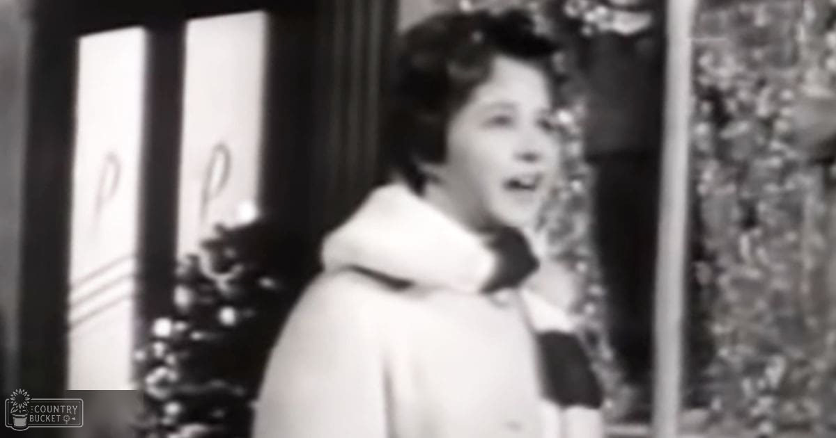 A young adult female wearing a white hoodie indoors with decorative elements visible in the background.