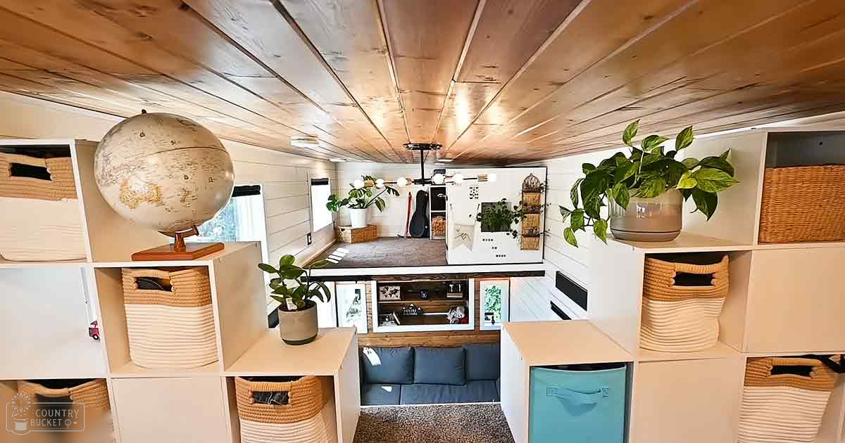 An indoor space with a globe on a wooden stand, potted plants, storage baskets and shelves filled with items, blue cushions on seating area, whiteboard with notes pinned to it.