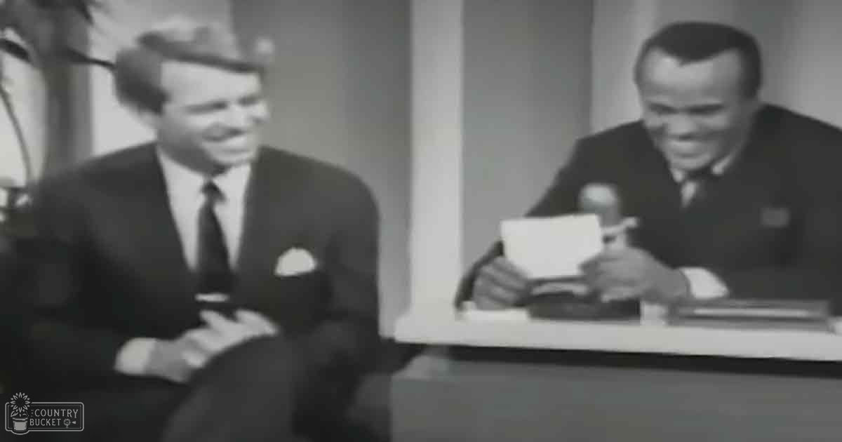 A mid-20th century television interview setting with two adult males dressed formally for business in a simple indoor studio environment.