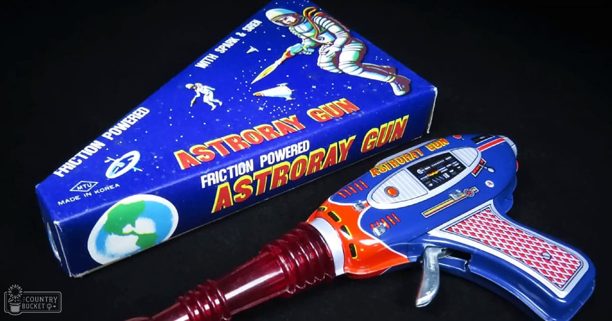 A toy Astroray Gun with a blue body, red handle, silver trigger, and illustrations of astronauts and space themes. The packaging is also blue with white text and images related to space exploration.