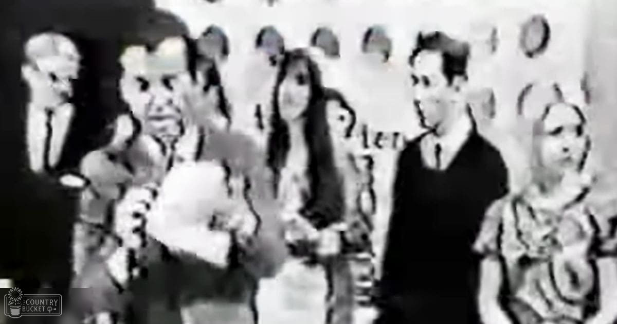 An adult male holding a trophy or award in front of children and other adults during what appears to be an indoor educational setting, possibly a classroom.