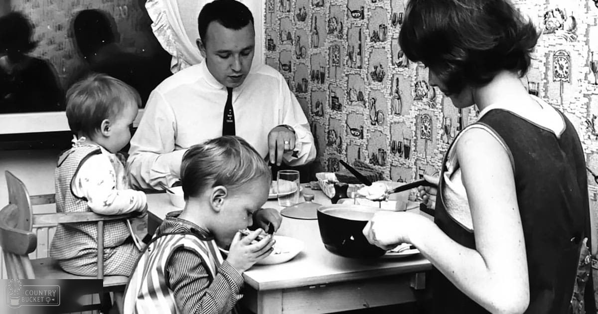 A family dining together at a wooden table in their home, with patterned wallpaper and mid-20th-century decor.