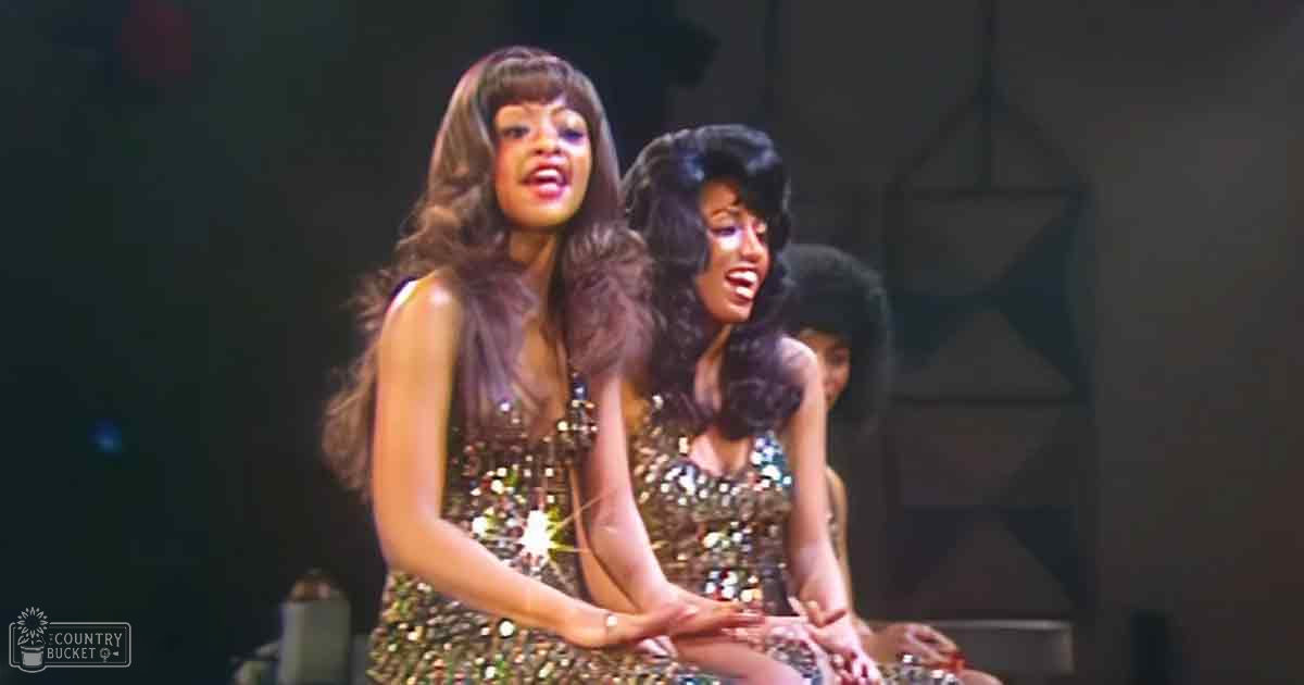 Two young adult female performers wearing sparkly sequined dresses with stage lighting indoors, likely a theater or performance venue.