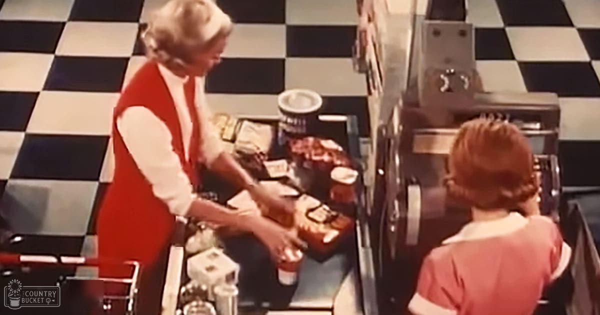 A middle-aged woman in a red sleeveless top and a child in an American-style mid-20th-century diner with metal counters, cash register, and checkered floor.