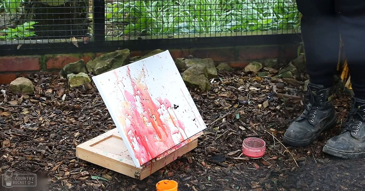 Abstract painting on wooden easel outdoors; wire fence, greenery, spring or summer day with natural light