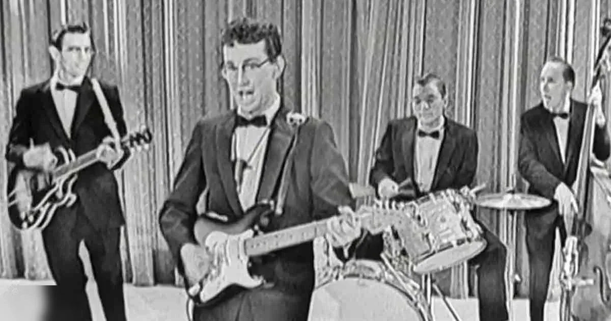 Young adult males in formal suits playing guitar in a studio setting with a curtain backdrop.