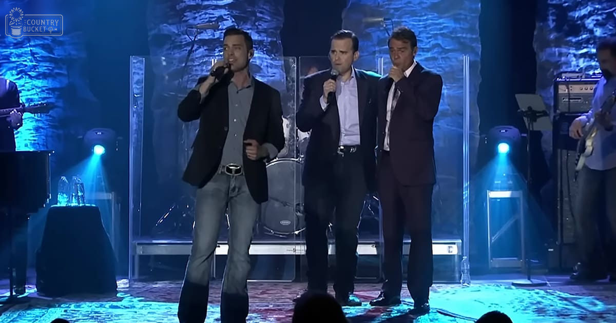 Adult males performing on stage under dramatic indoor lighting with microphones and guitars visible.