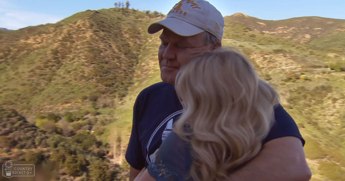 Middle-aged man holding young adult woman outdoors with green hills and clear blue sky, spring or summer day