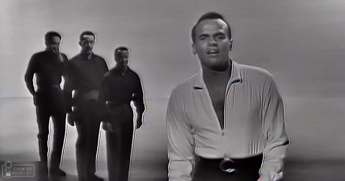 An adult male in a light-colored long-sleeved shirt with a collar and zipper details stands in the foreground against a plain, light-colored wall.