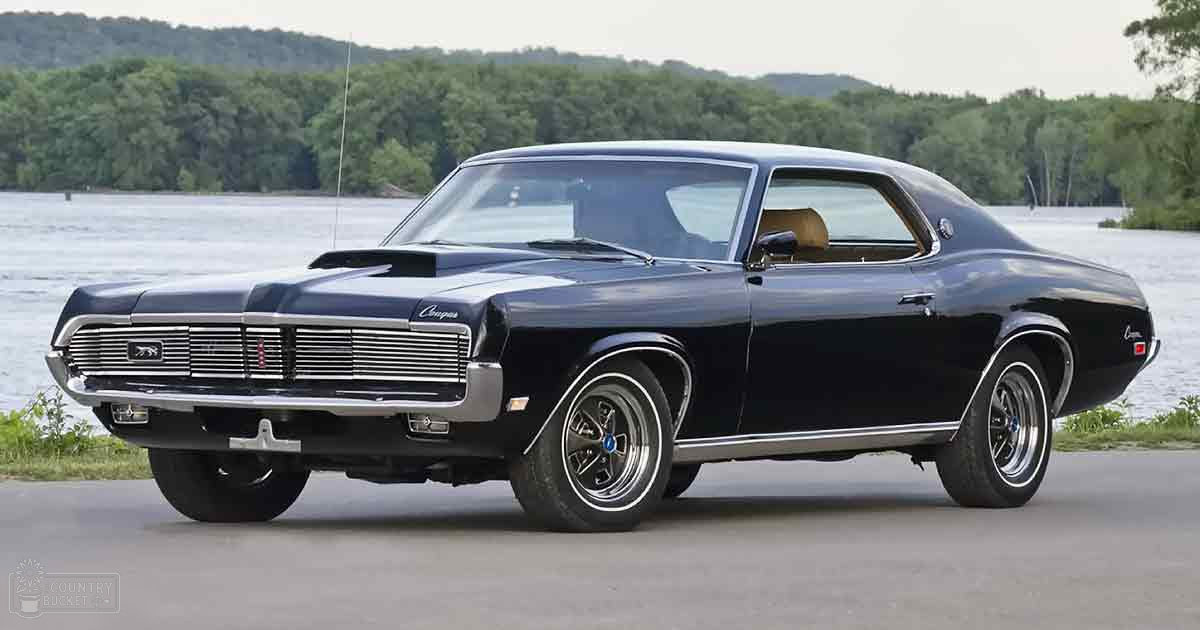 Black Mercury Cougar muscle car parked near a body of water with overcast skies in late spring or early fall.