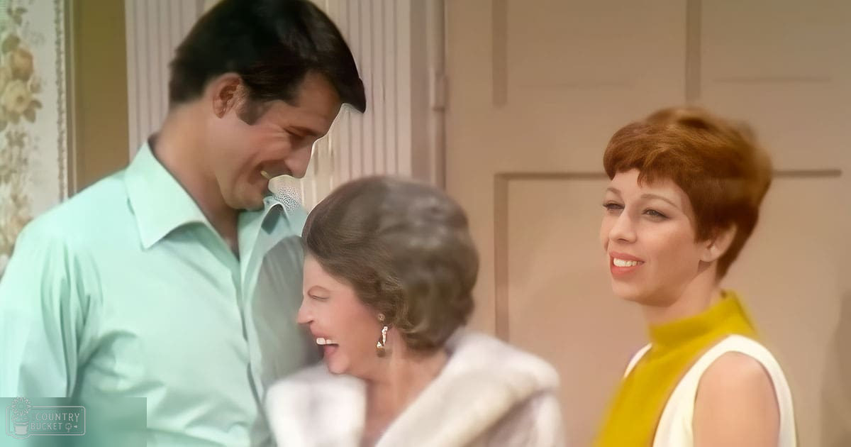 A family scene indoors with three adults from different age bands, dressed in mid-20th century attire with a floral-patterned curtain and panelled door suggesting a residential setting.