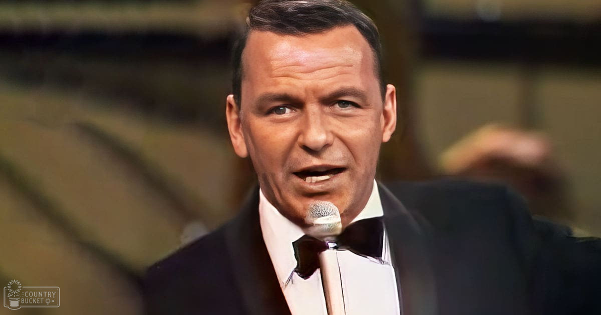 A middle-aged man wearing a formal tuxedo with bow tie stands indoors, likely in an auditorium or stage setting.
