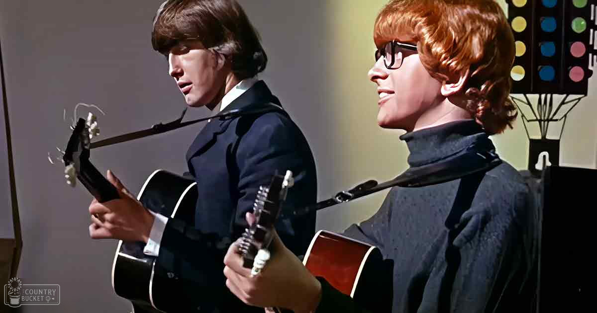 Musical performance scene with young adult males in formal and casual attire, microphone stand and decorative panel in an indoor stage setting.