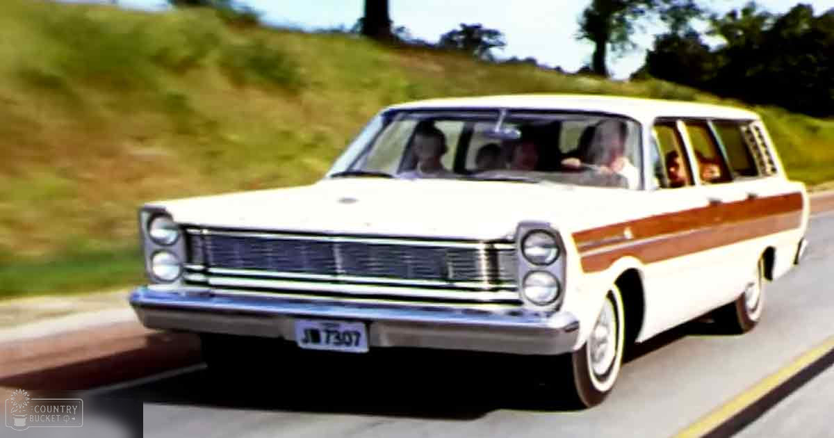 A vintage station wagon with white body, wood paneling, and chrome details, parked on a paved road surrounded by greenery in a rural area under clear skies with some clouds visible.