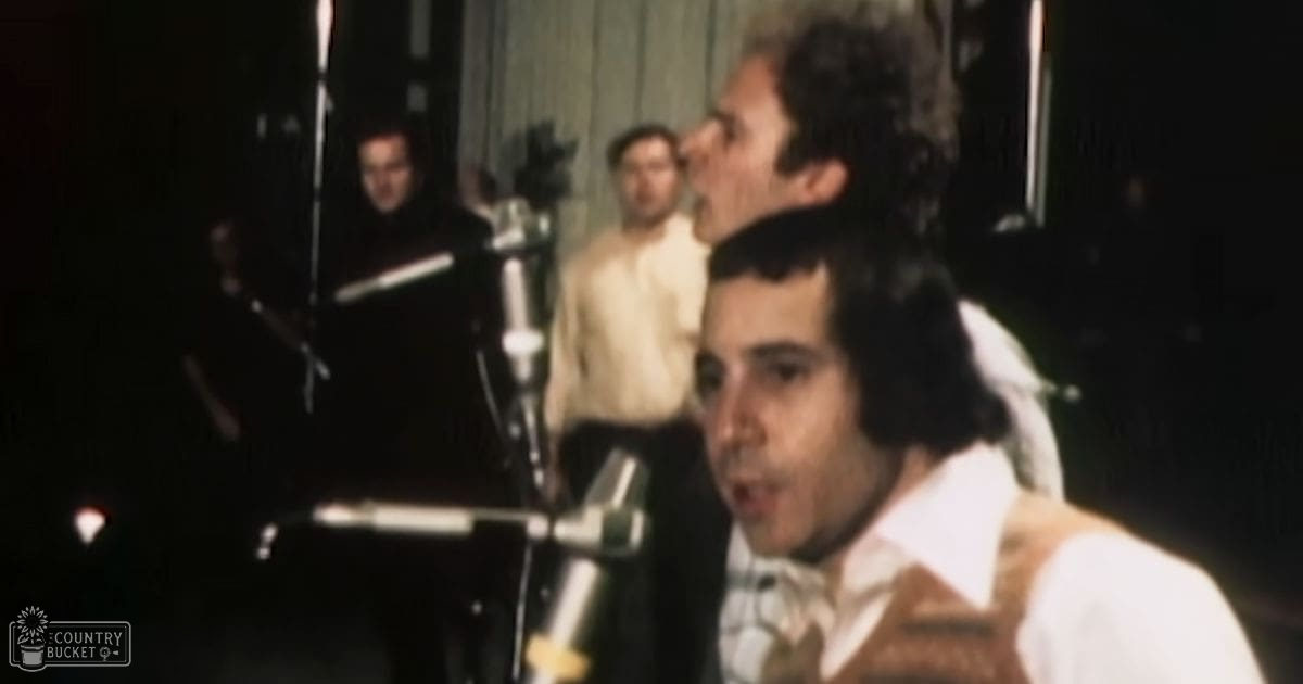 Recording session in a studio setting with individuals wearing 1970s fashion styles, microphones prominent, curtains for background, indoor lighting setup.