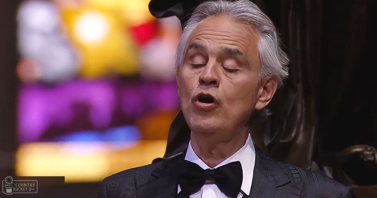 A middle-aged adult male in a tailored black tuxedo with subtle embroidery, wearing a bow tie and white dress shirt, stands indoors under warm stage lighting at what appears to be a formal event.