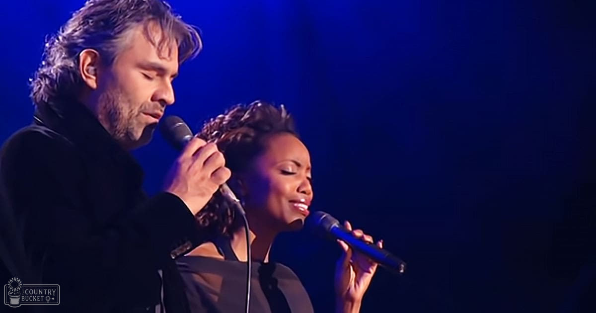 Duet performance scene at an indoor concert venue with microphones on stage, blue lighting suggests evening.