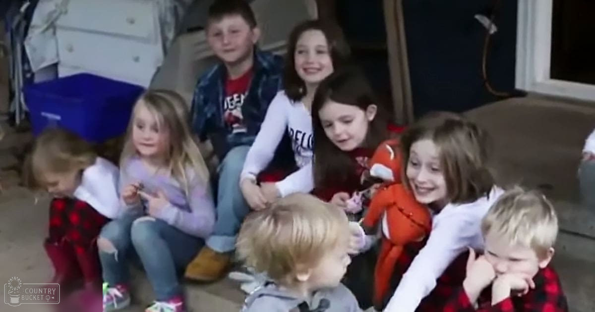 Six children in a playroom with red plaid skirts, white long-sleeve tops, and blue plaid shirts. Natural light illuminates the indoor setting.