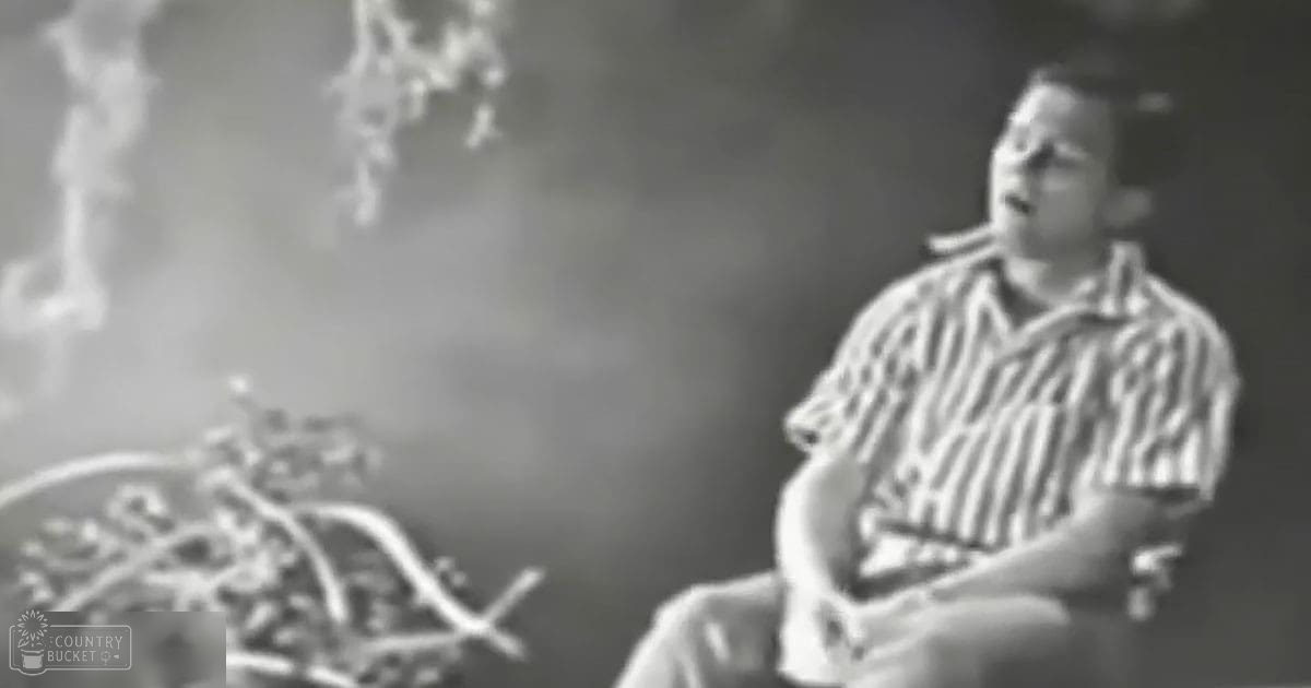 An adult male seated indoors with a striped shirt, dimly lit evening scene.