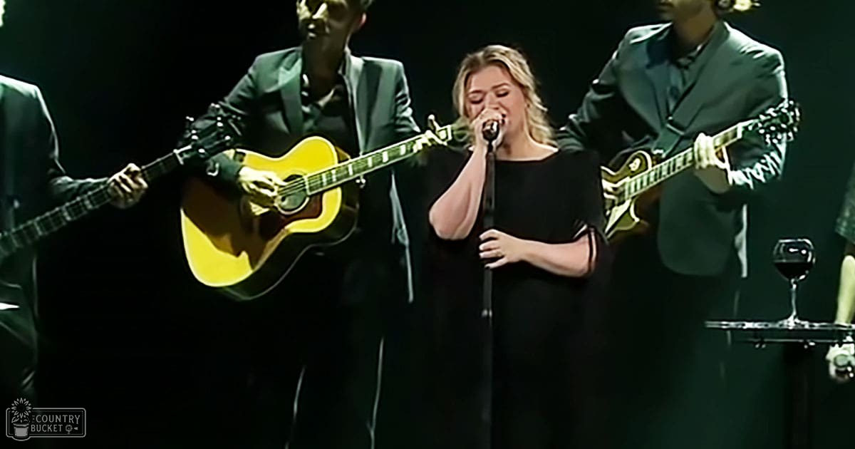 A live concert scene with a female singer performing alongside male musicians holding guitars; a glass of red wine is visible in the background, indicating an indoor setting.
