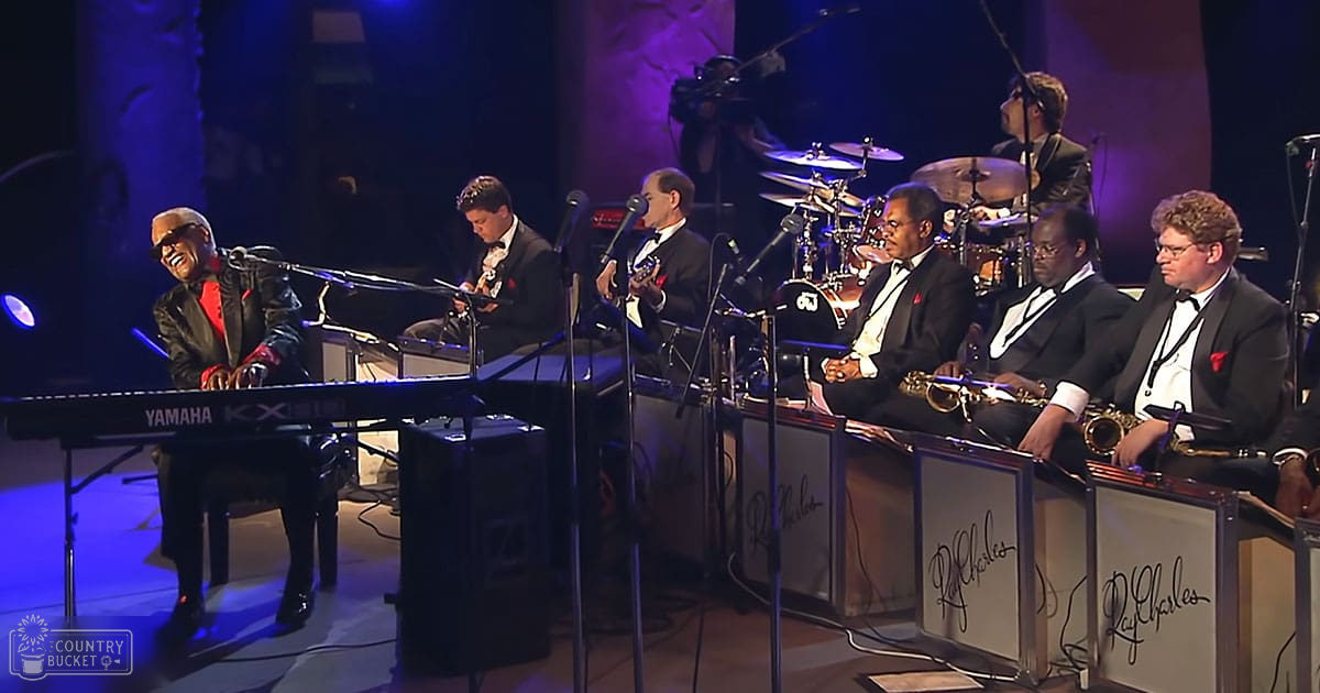 Ray Charles performing at an indoor concert with a band in dark suits and stage lighting primarily in blue and purple hues.